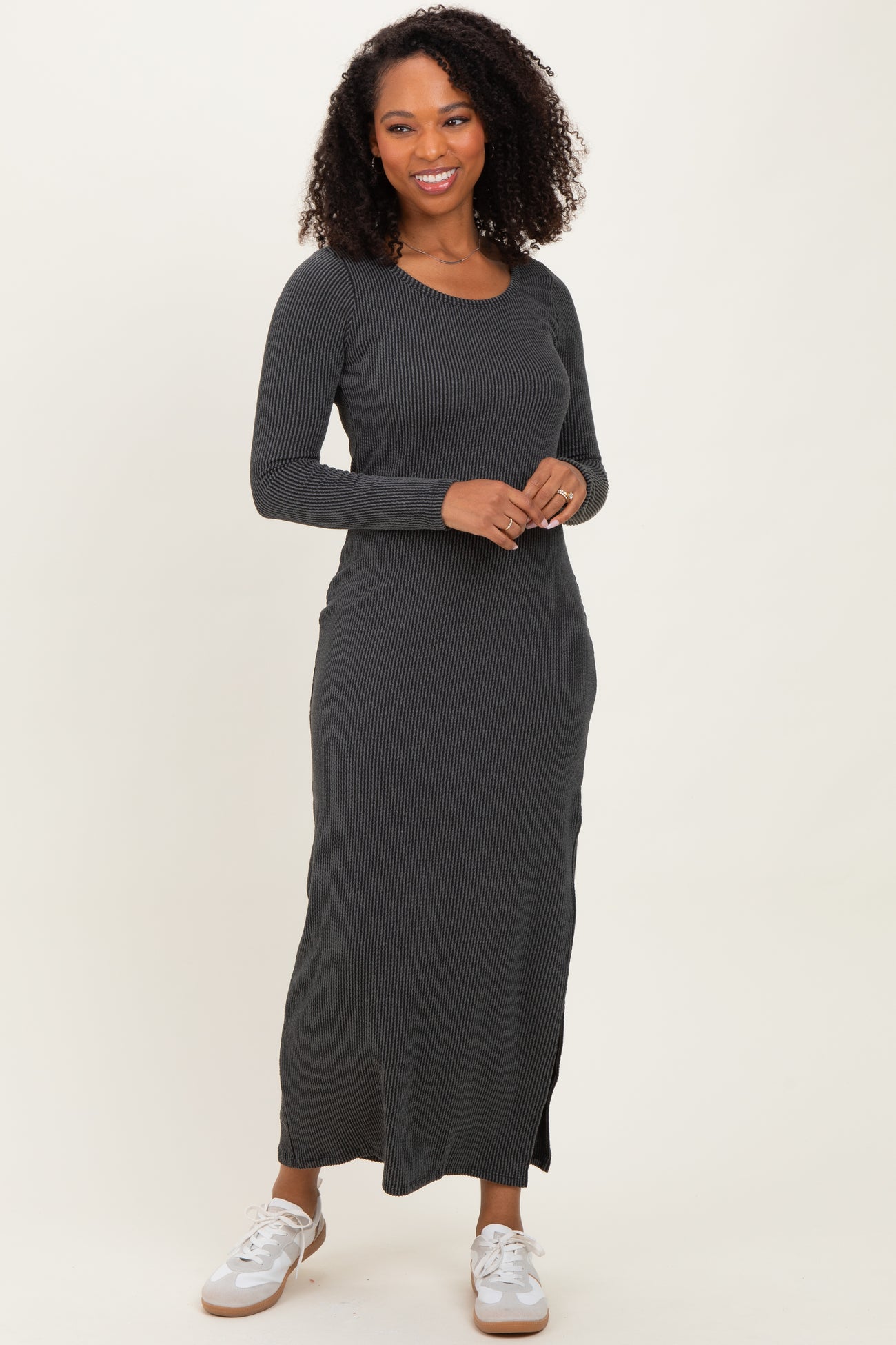 woman wearing a black ribbed long sleeve maxi dress with a round neckline and side slits, paired with white sneakers