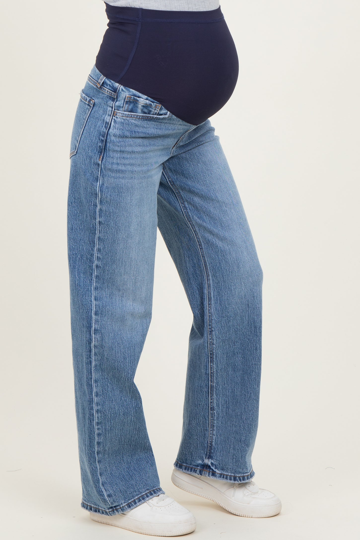 woman wearing light blue maternity jeans with a navy belly panel and standing with a baby bump visible