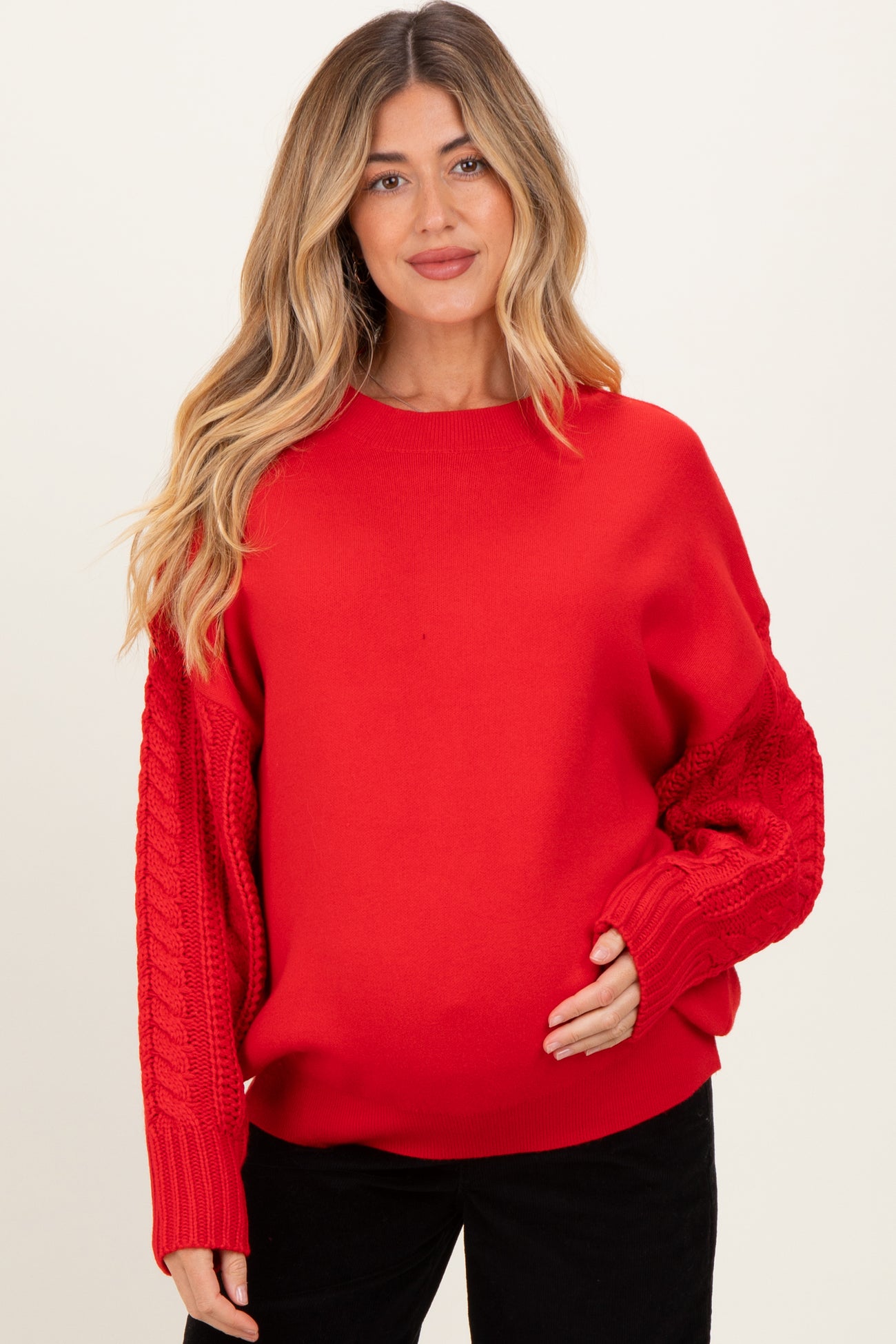 woman wearing a red maternity sweater with cable-knit sleeves and visible baby bump