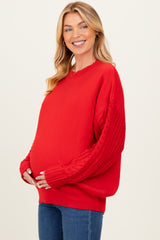 woman wearing a red maternity sweater with cable knit sleeves and holding her baby bump