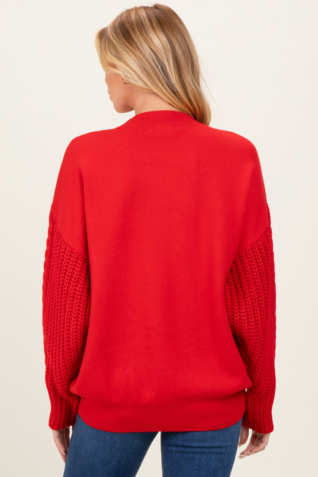 woman wearing a red oversized maternity sweater with textured knit sleeves and a relaxed fit from the back