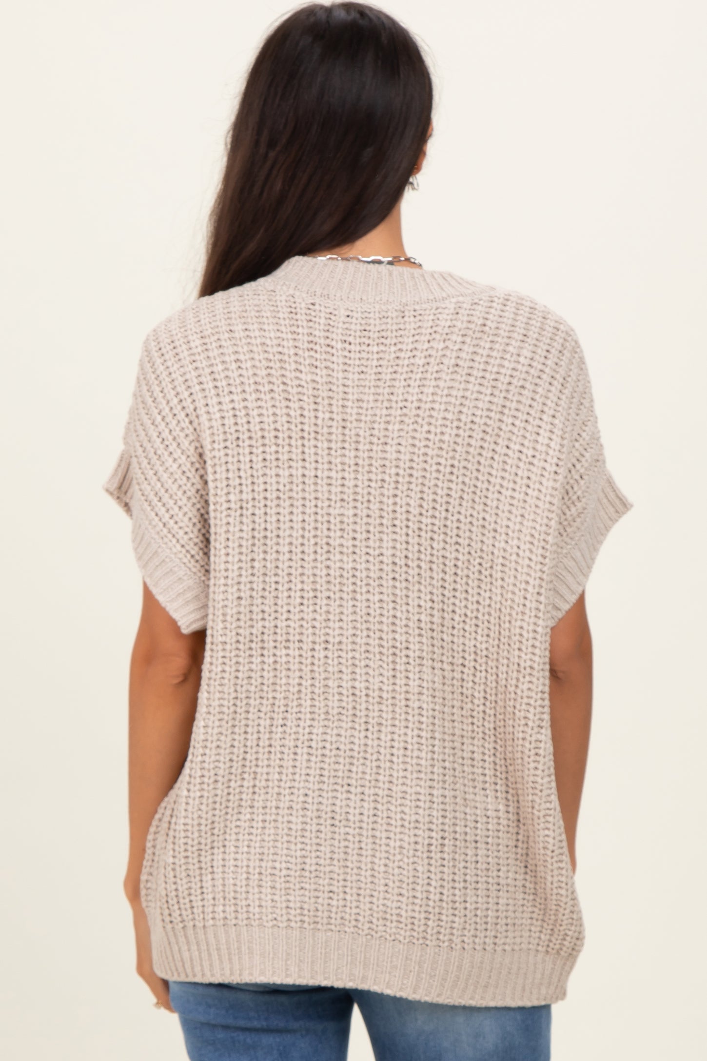 woman wearing a beige knitted oversized sweater from the back, paired with blue jeans