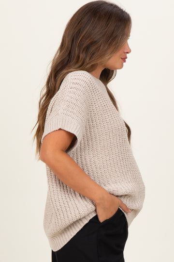woman wearing a light beige short sleeve maternity sweater with a loose fit and side pockets, showcasing her baby bump
