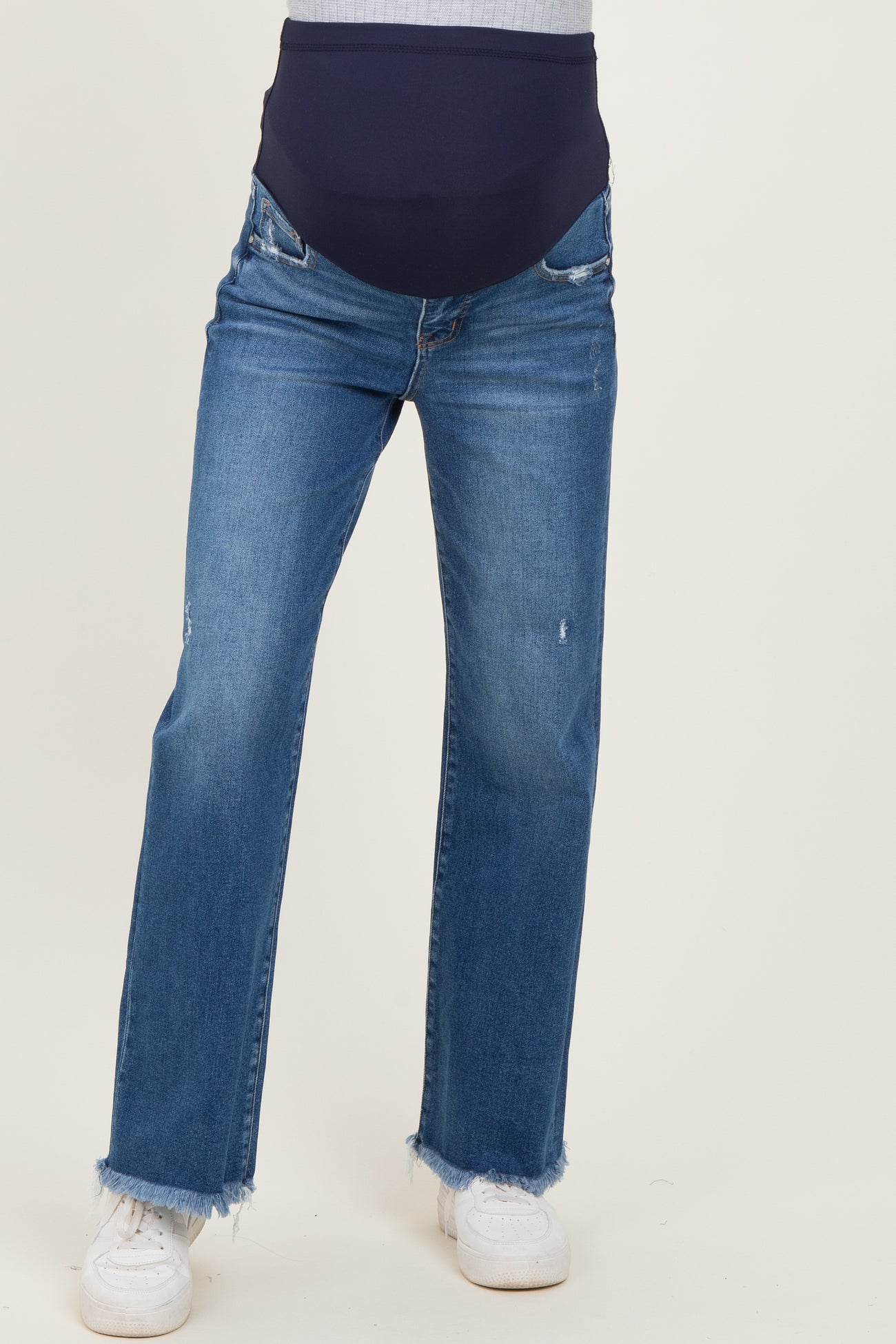 woman wearing maternity distressed straight leg jeans with a dark blue over-the-bump waistband and white sneakers