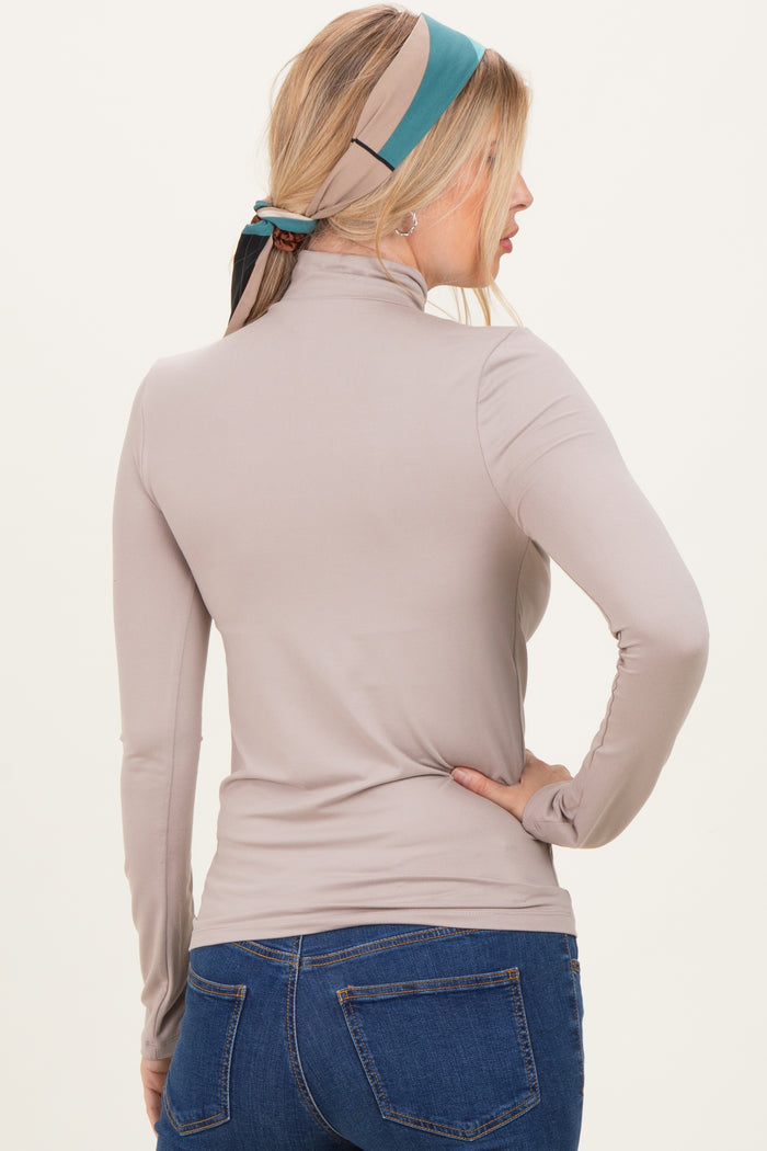 woman wearing a taupe long sleeve mock neck top paired with blue jeans, view from the back