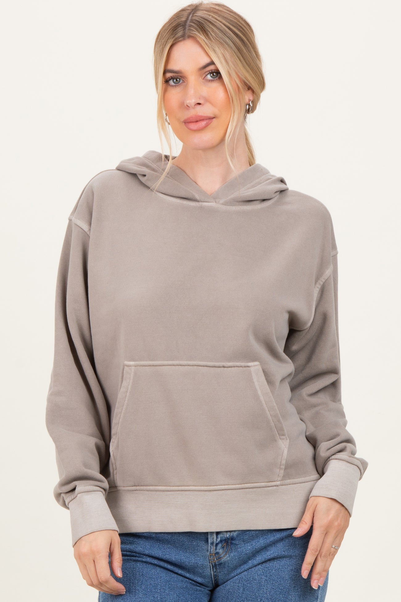 woman wearing a tan oversized hoodie with a front pocket and adjustable drawstring hood