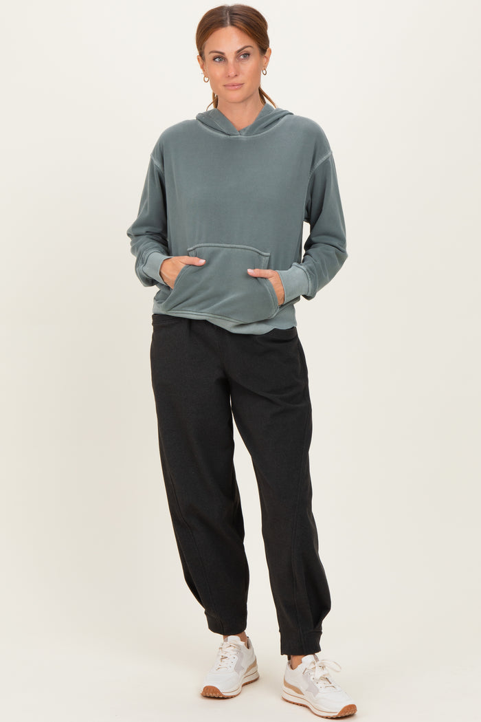 woman wearing a green hooded sweatshirt with a front pocket and black jogger pants, paired with white sneakers