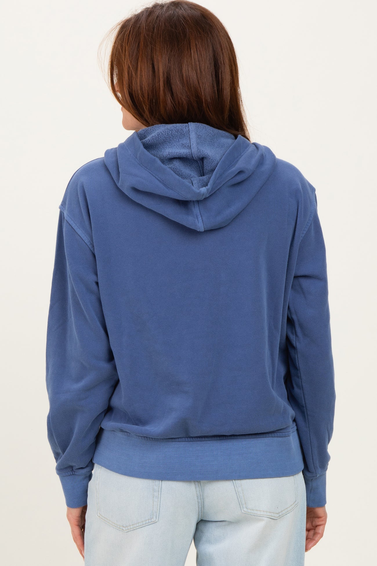 woman wearing a blue hooded sweatshirt, showing the back view with a relaxed fit and ribbed hem.