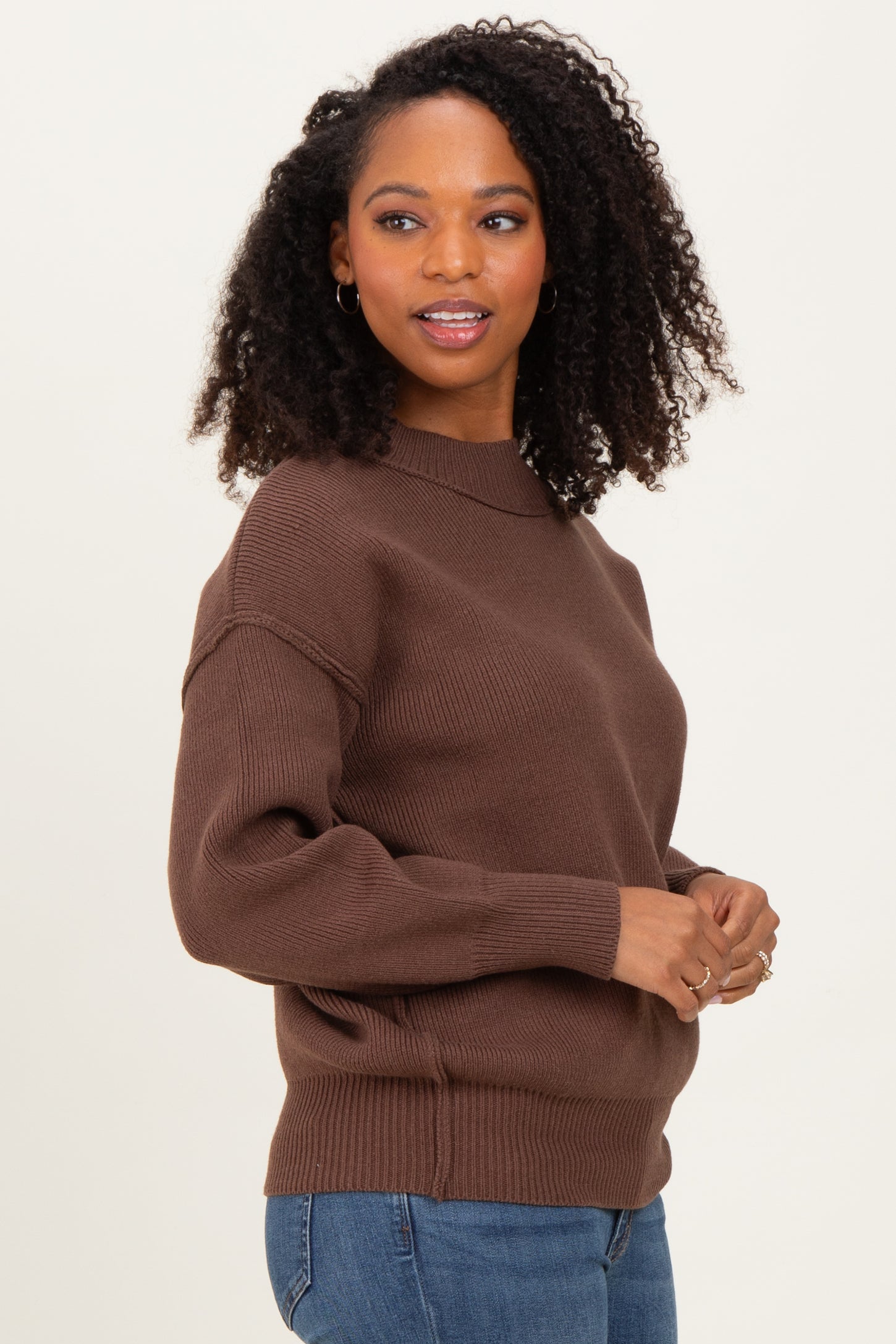 woman wearing a brown rib knit sweater with a high neckline and long sleeves, styled with blue jeans