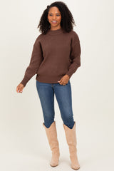 woman wearing a brown oversized knit sweater and blue skinny jeans, standing in tan knee-high boots