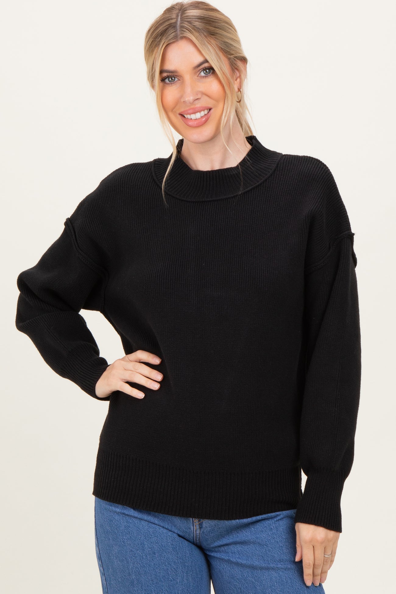 woman wearing a black knitted sweater with a relaxed fit and high neck, paired with blue jeans