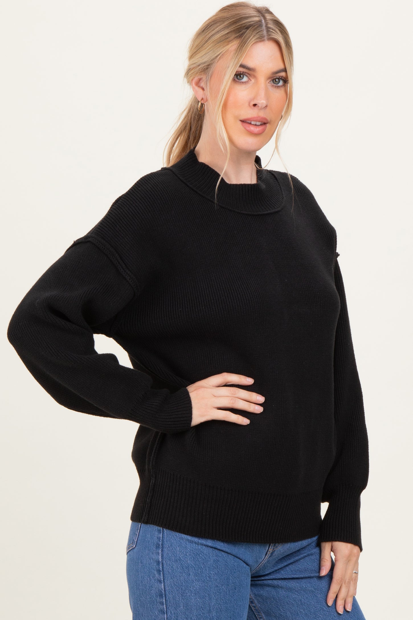 woman wearing a black oversized sweater with a round neckline and long sleeves, paired with blue jeans