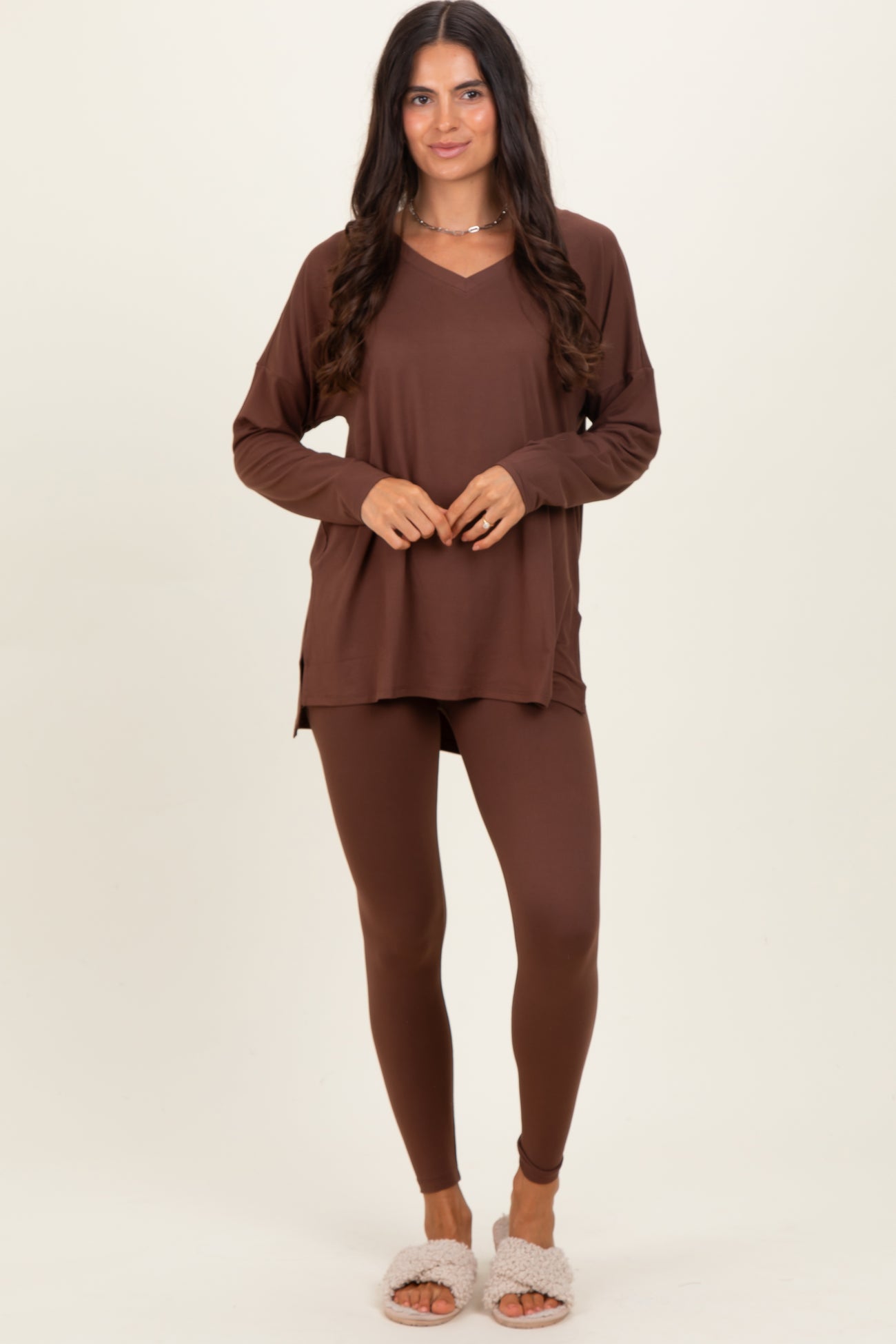 woman wearing a brown long sleeve top with a v-neck and brown leggings, styled with fluffy slippers