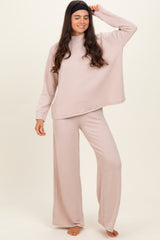 woman wearing a light pink ribbed long sleeve top and matching wide-leg pants, standing barefoot with a playful pose