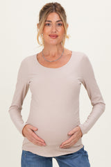 woman wearing a light beige long sleeve maternity top and holding her baby bump