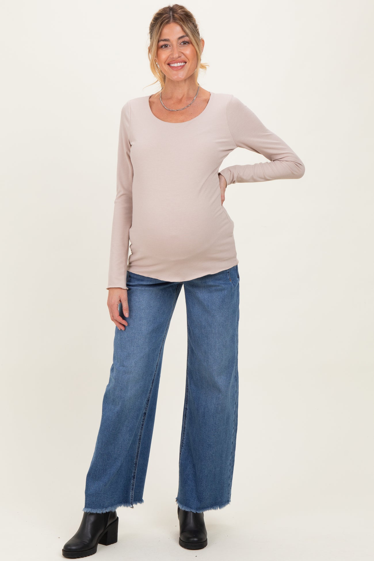 woman wearing a light beige long sleeve maternity top and blue wide leg jeans, showing her baby bump