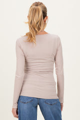 woman wearing a light taupe long sleeve maternity top with gathered waist detail and blue jeans
