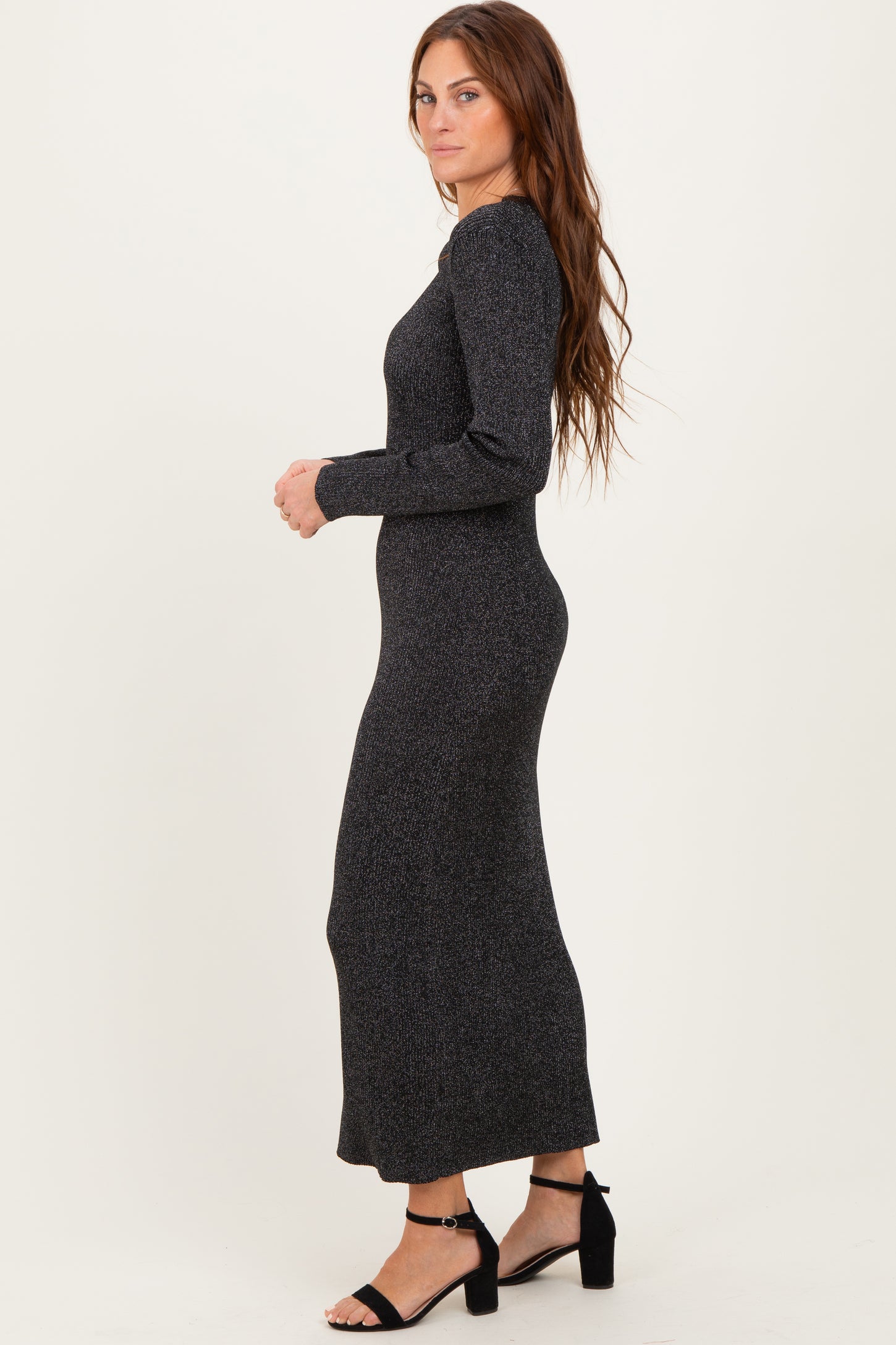 woman wearing a fitted black long sleeve maxi dress with a textured pattern and strappy black heels