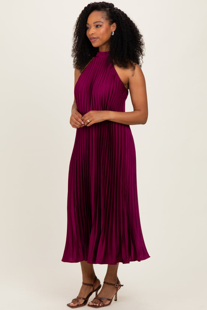 woman wearing a sleeveless pleated midi dress in deep burgundy with a halter neck and styled curls