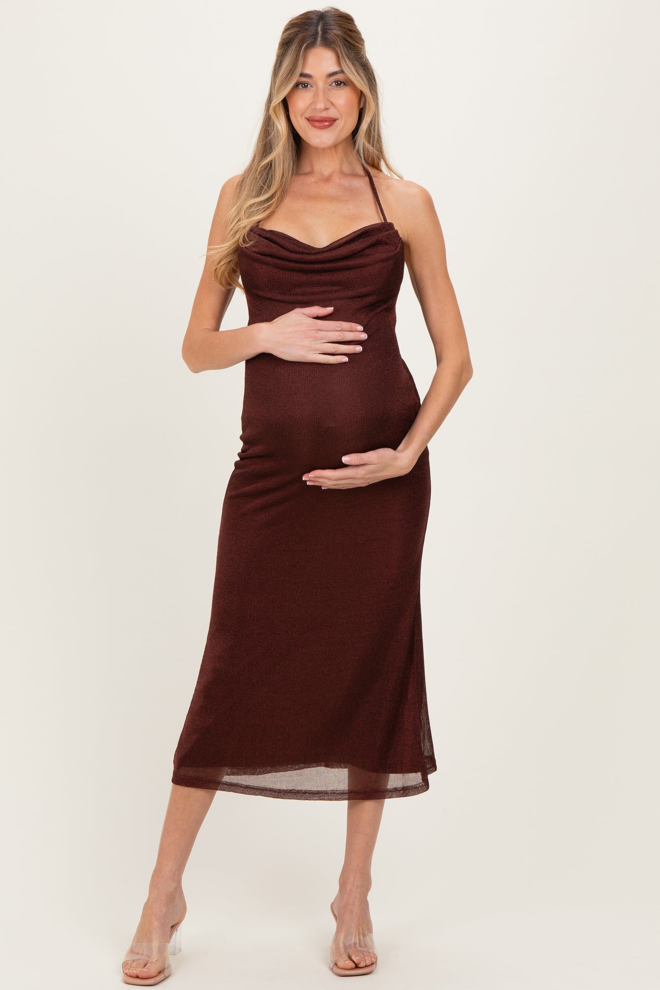 woman wearing a burgundy maternity dress with a cowl neckline and halter straps, holding her baby bump