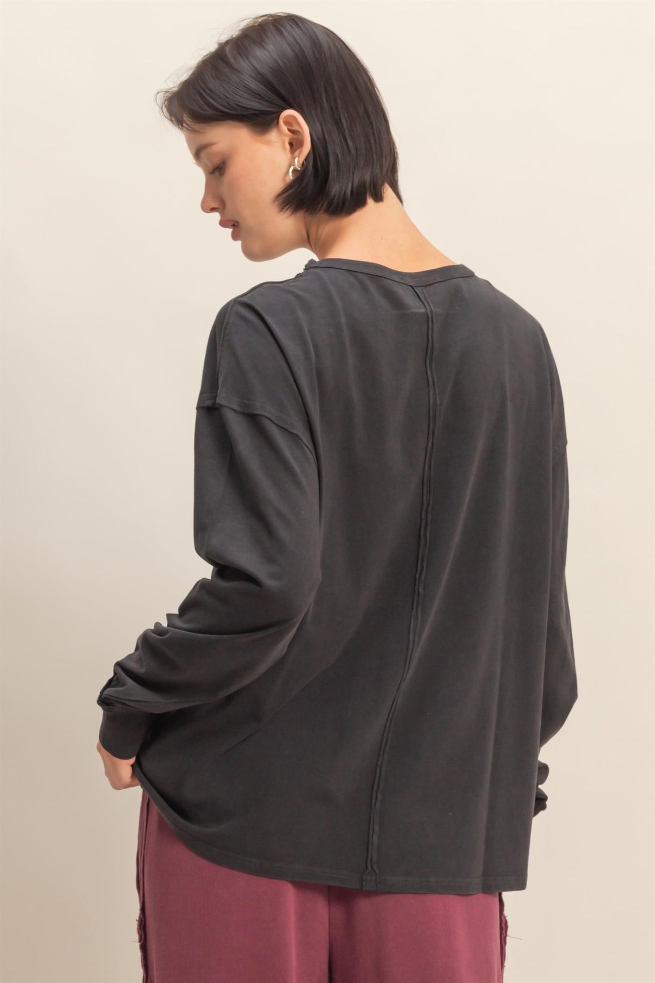woman wearing a dark gray long sleeve oversized top, showing the back with a relaxed fit and stitched detailing