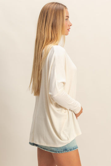 woman wearing a white long sleeve oversized top with a relaxed fit and light blue denim shorts