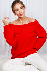 woman wearing a red off-the-shoulder sweater with long sleeves and a relaxed fit, sitting against a light backdrop