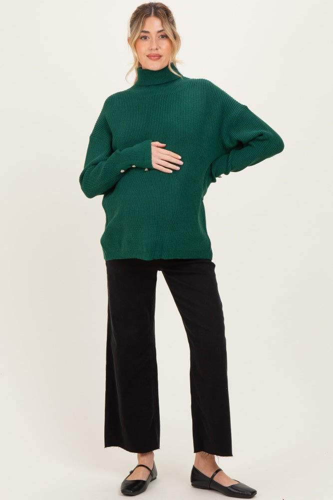 woman wearing a green maternity turtleneck sweater and black wide-leg pants, with a visible baby bump