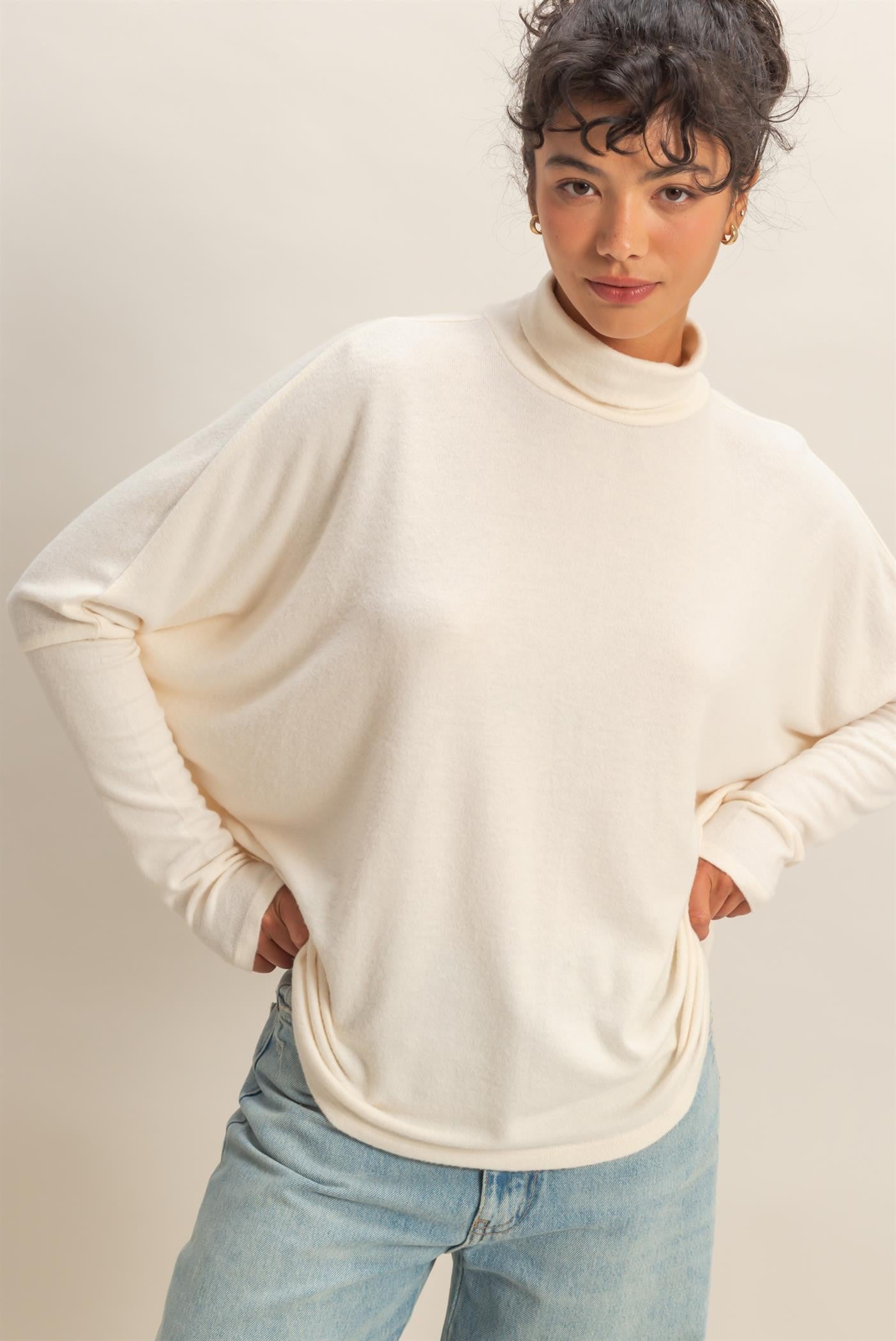 woman wearing a cream oversized turtleneck sweater with relaxed fit and light blue jeans