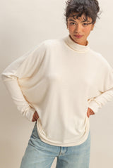 woman wearing a cream oversized turtleneck sweater with relaxed fit and light blue jeans