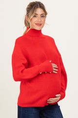woman wearing a red maternity sweater with a turtleneck and button details, gently cradling her baby bump