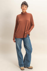 woman wearing a rust-colored long sleeve turtleneck top with relaxed fit and blue wide-leg jeans