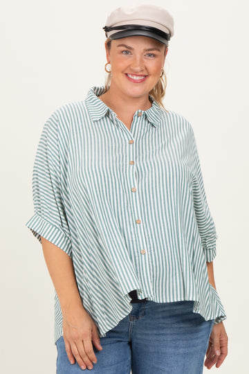 woman wearing a green and white striped maternity plus button-up shirt with rolled sleeves and a playful smile