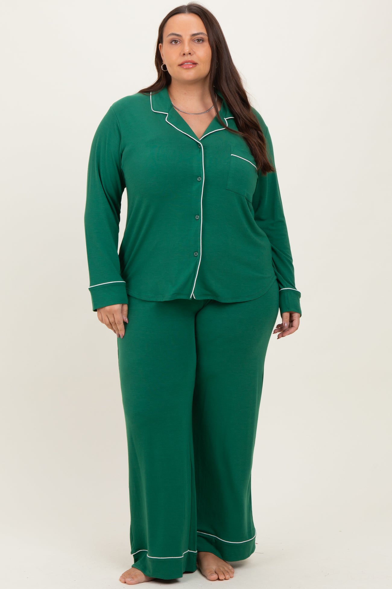 woman wearing a green plus size two-piece pajama set with long sleeves and pants, featuring white piping details