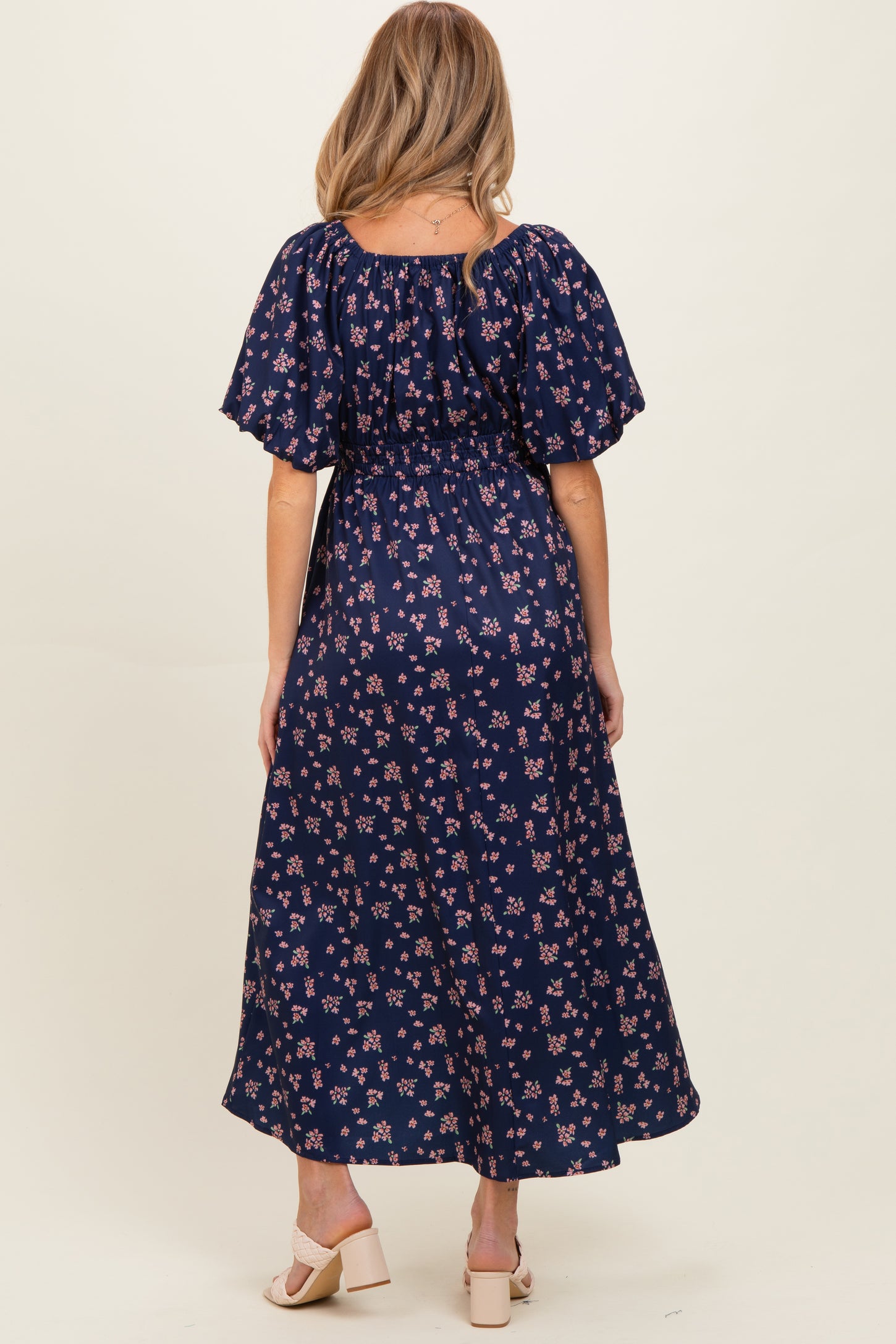 woman wearing a navy blue floral print maternity dress with puff sleeves and a fitted waist, viewed from the back