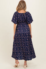 woman wearing a navy blue floral print maternity dress with puff sleeves and a fitted waist, viewed from the back