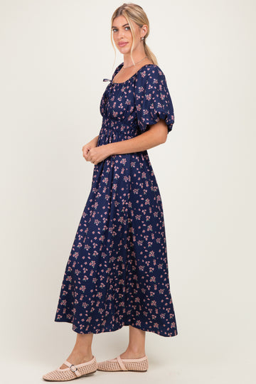 woman wearing a navy blue floral maxi dress with puff sleeves and a square neckline, standing in profile