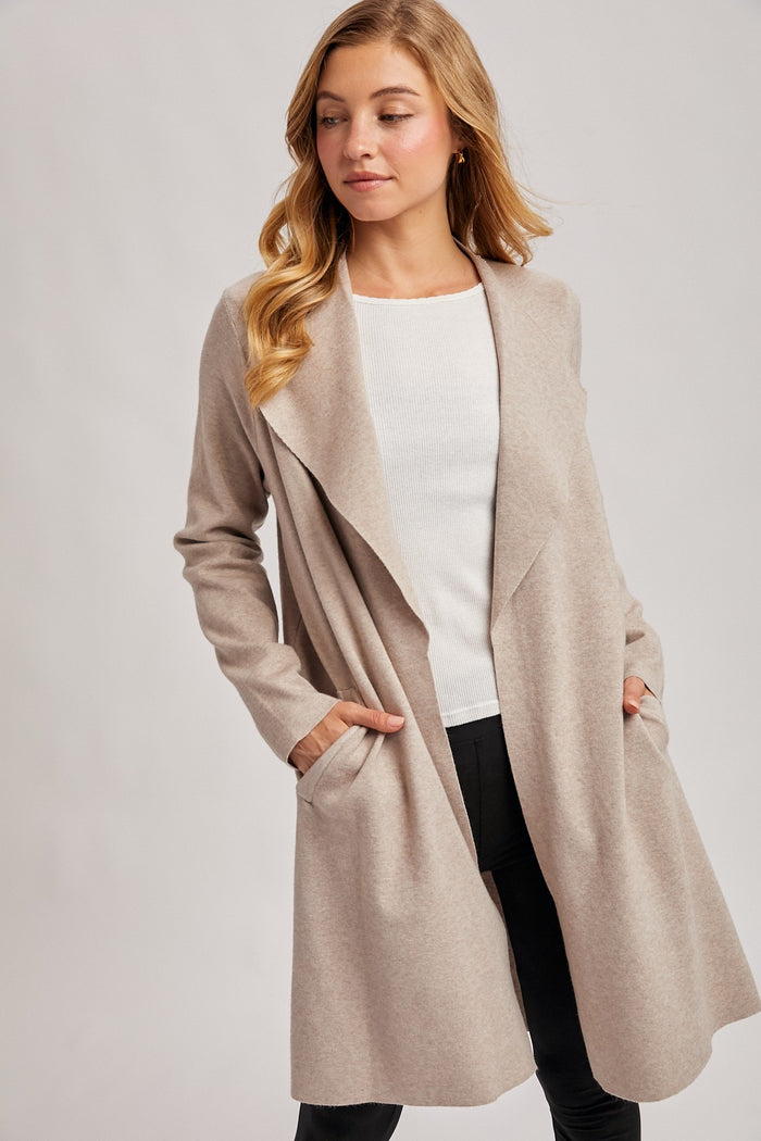 woman wearing a beige long cardigan with open front and pockets over a white top and black pants