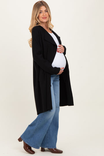 woman wearing a black long maternity cardigan and holding her baby bump while dressed in flared jeans and boots