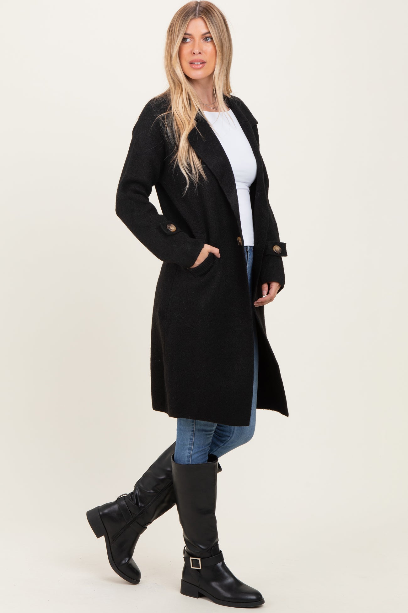 woman wearing a black long coat over a white top, blue jeans, and black knee-high boots