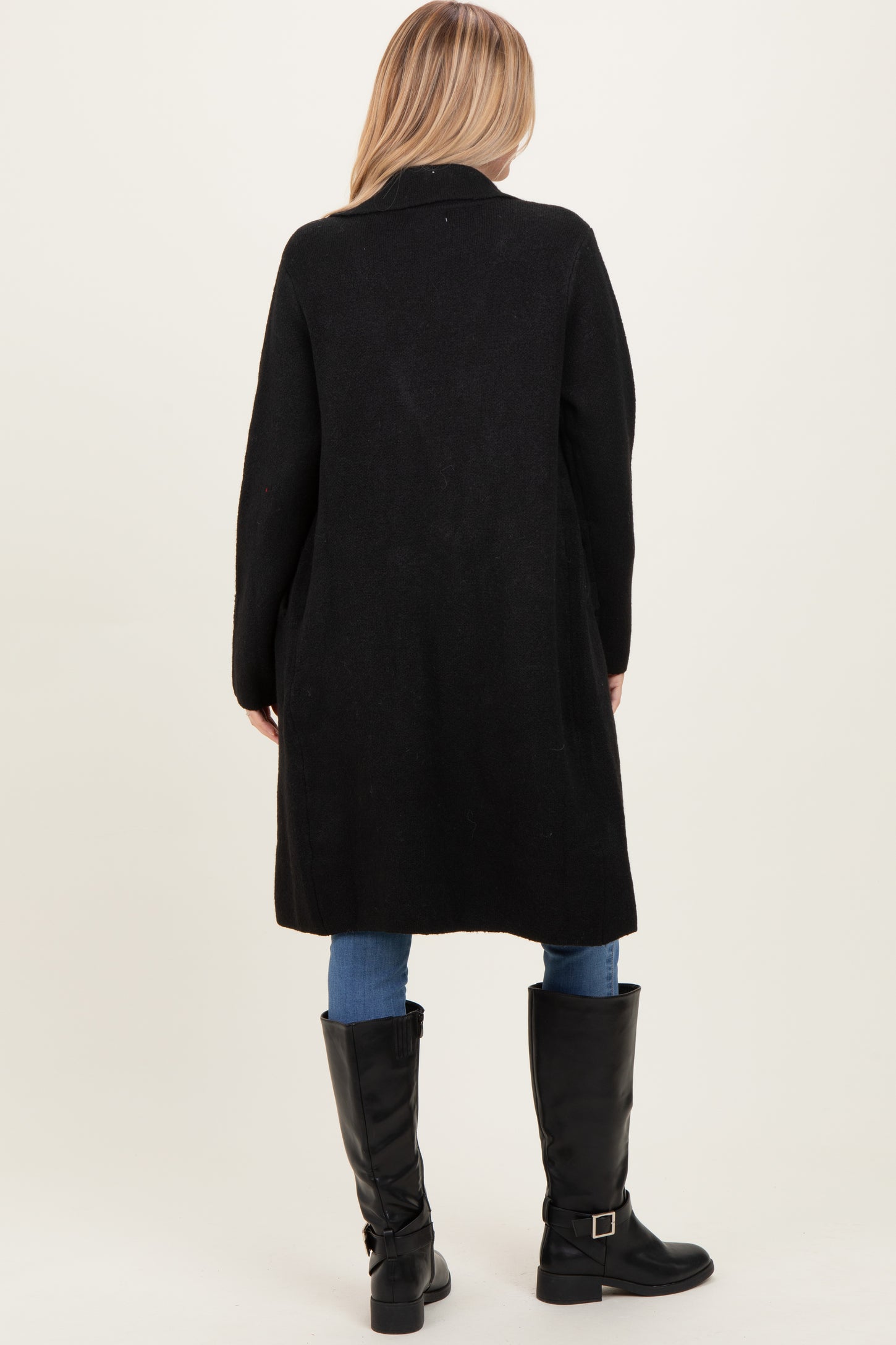 woman wearing a long black cardigan, back view, paired with blue jeans and knee-high black boots