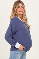 woman wearing a navy blue ribbed maternity sweater with white cuffs and a visible baby bump
