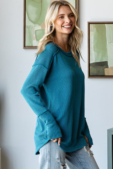 woman wearing a teal oversized waffle knit sweater with long sleeves and relaxed fit, paired with distressed jeans