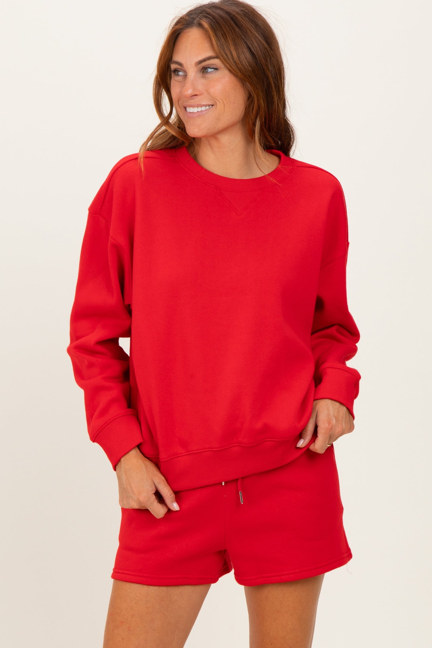 woman wearing a red oversized sweatshirt with long sleeves and a crew neckline, paired with matching shorts