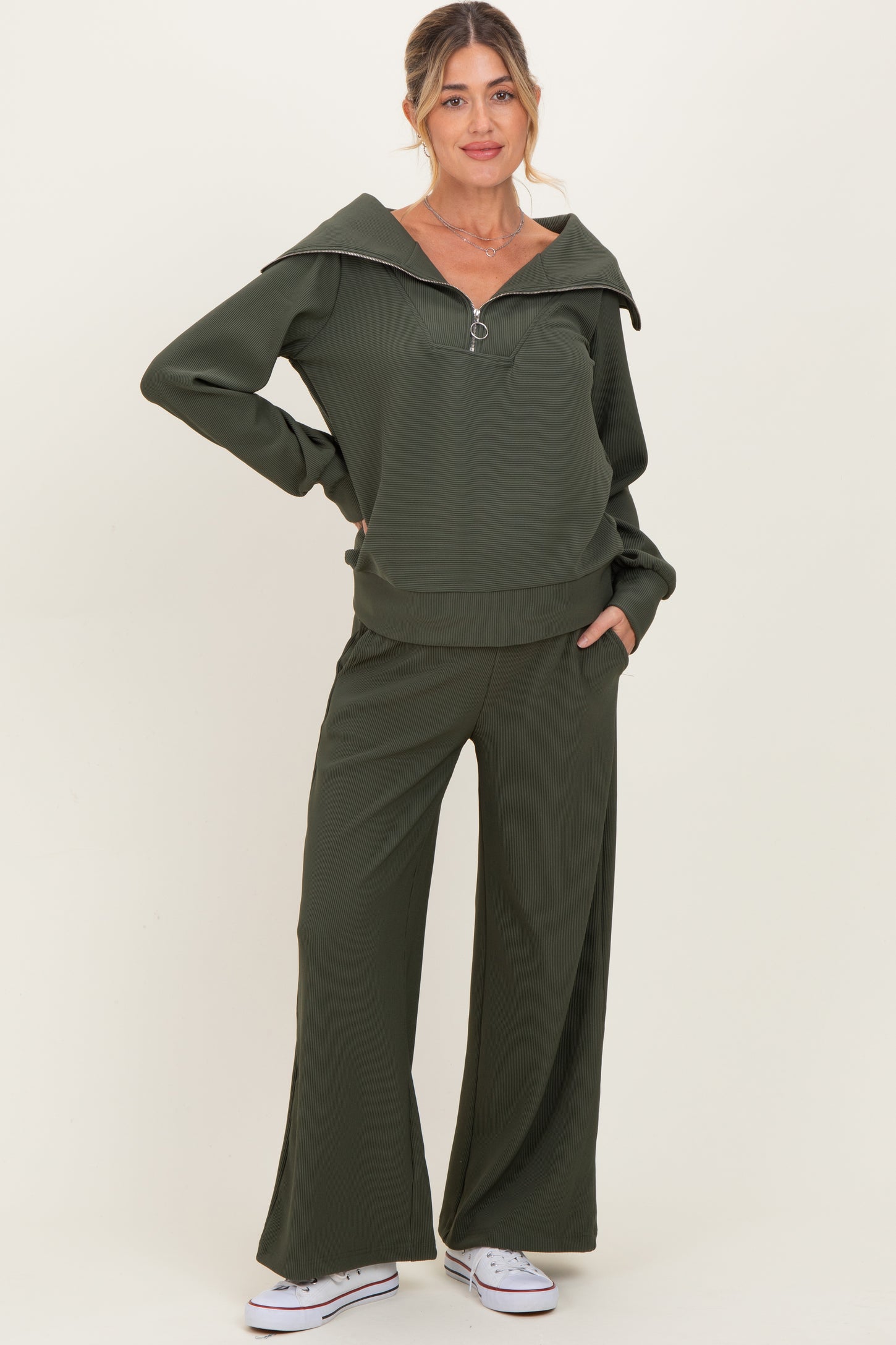 woman wearing an olive green maternity zip-up sweater and matching wide-leg pants