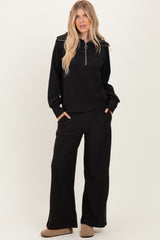 woman wearing a black long sleeve zip-up top with a collar and matching wide-leg black pants.