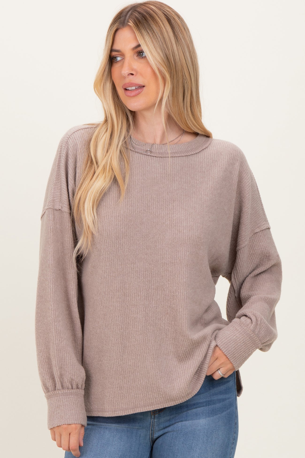 woman wearing a taupe ribbed long sleeve top with a relaxed fit and balloon sleeves paired with blue jeans