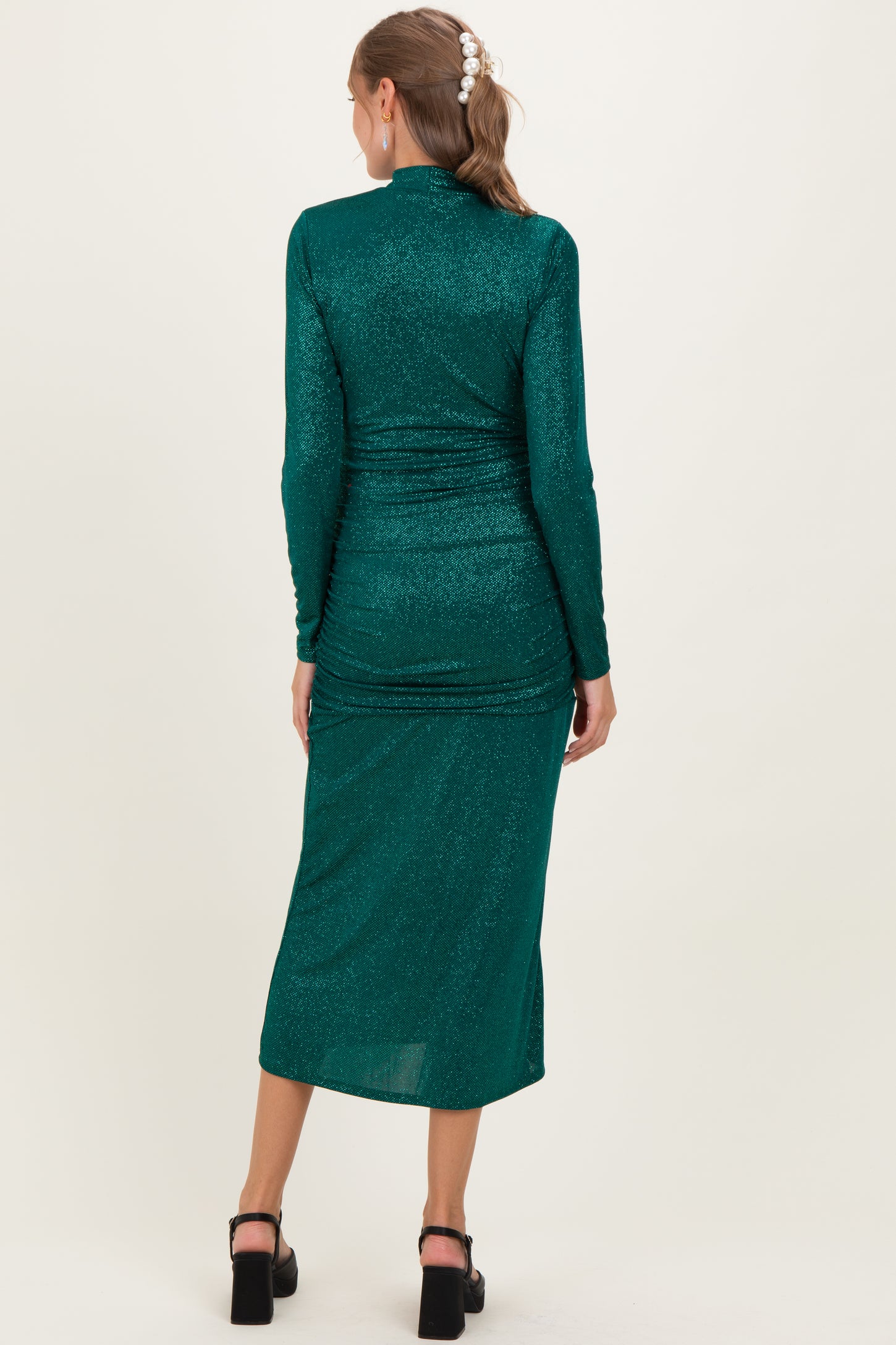 woman wearing a green sparkly maternity dress with long sleeves and a fitted silhouette, showing a baby bump
