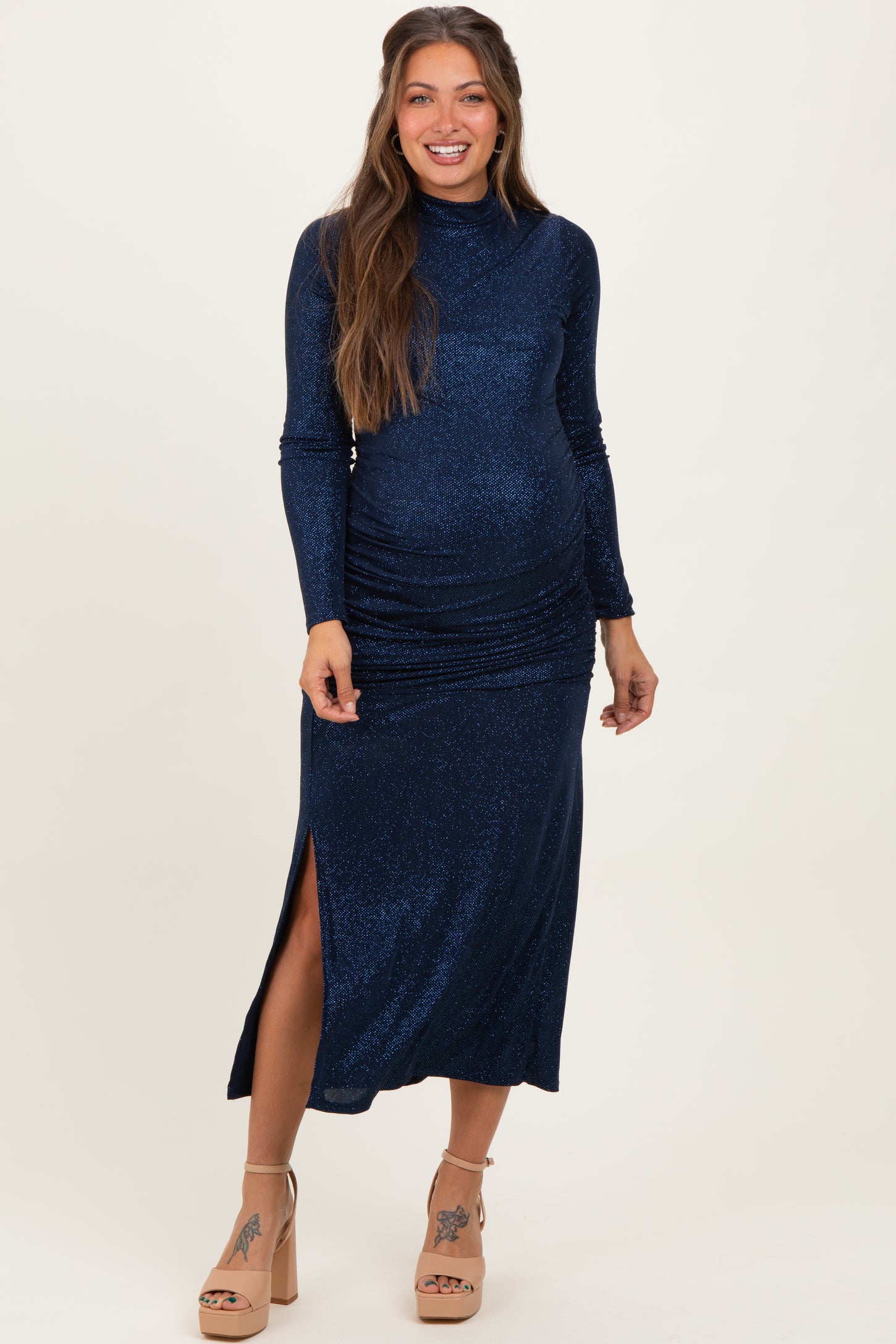 woman wearing a navy blue glittery maternity dress with long sleeves and a side slit, showing her baby bump