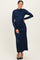 woman wearing a navy blue long sleeve shimmer maxi dress with ruching and a side slit, posing with one hand on her hip